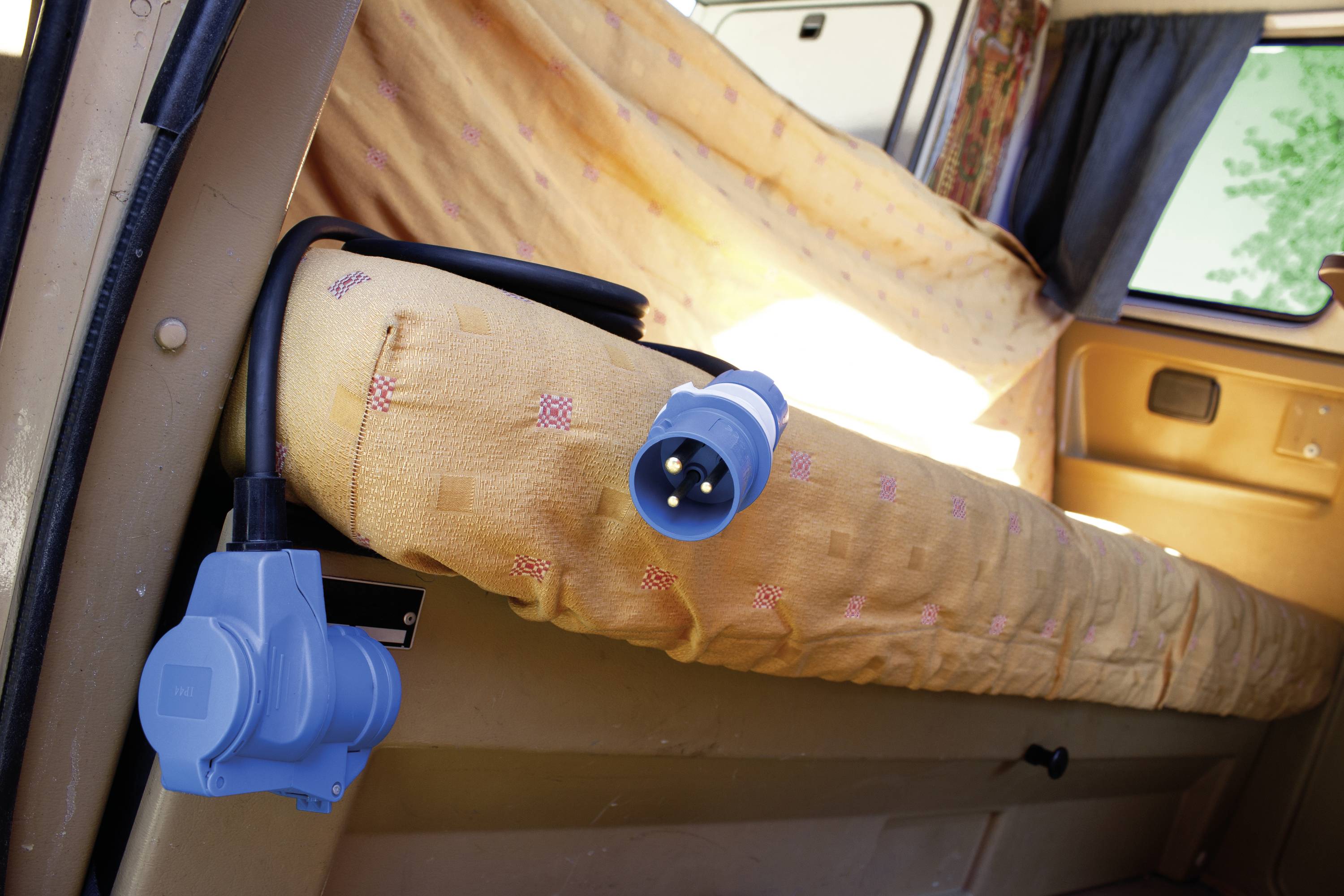 Une prise bleue est suspendue à un câble au-dessus d'un siège de voiture beige. Elle se trouve dans une portière ouverte, avec un rideau partiellement visible.