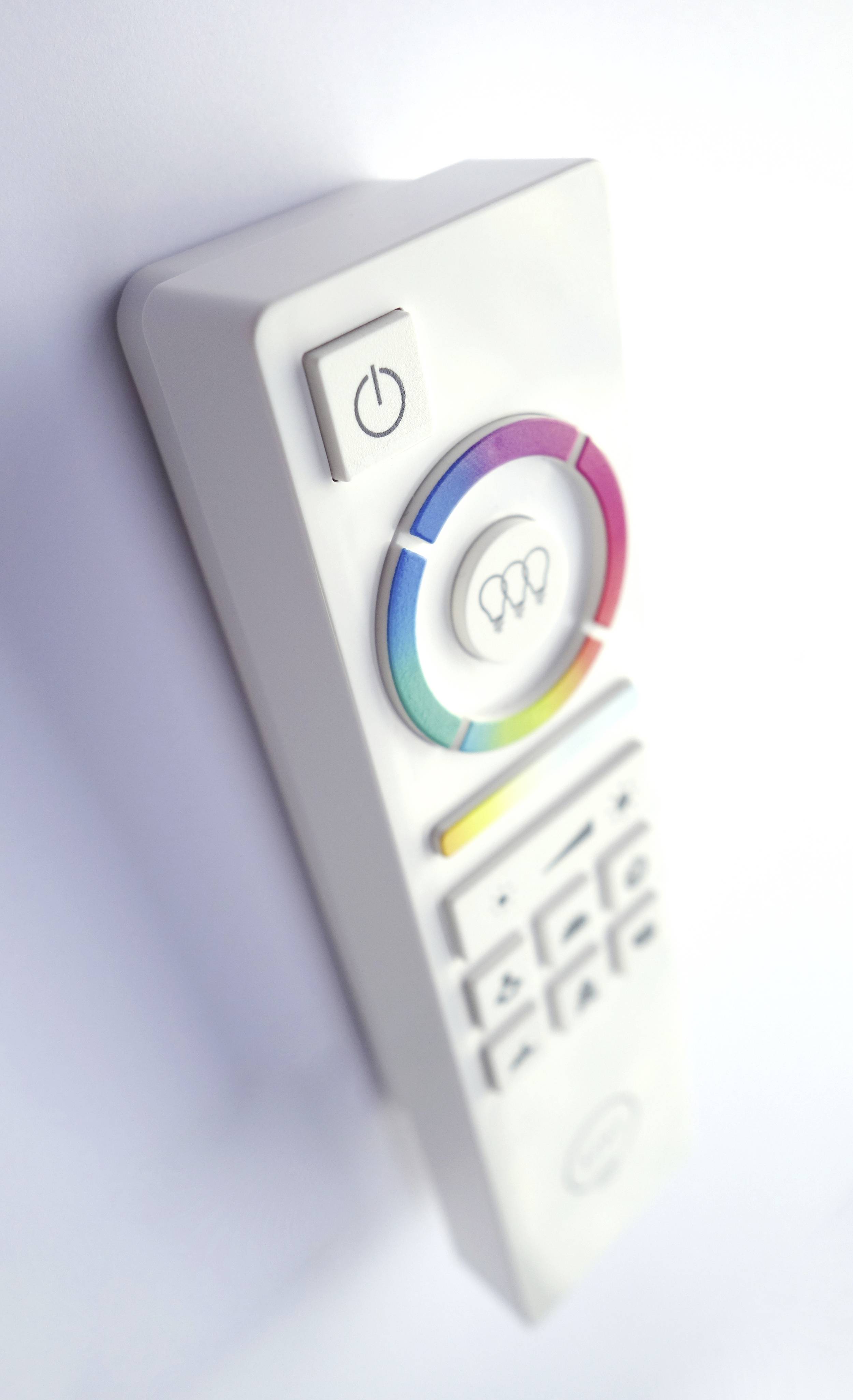 Télécommande blanche avec un cercle coloré et plusieurs touches, dont une grande touche Marche/Arrêt en haut.