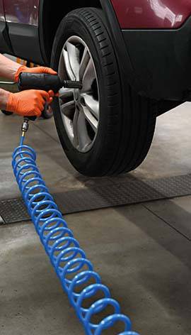 Une personne change un pneu de voiture avec une clé à chocs dans un atelier. Un tuyau d'air bleu est visible.