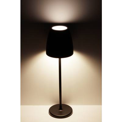 Une lampe de table noire sur un fond blanc brille intensément et projette une lueur douce vers le haut sur le mur.