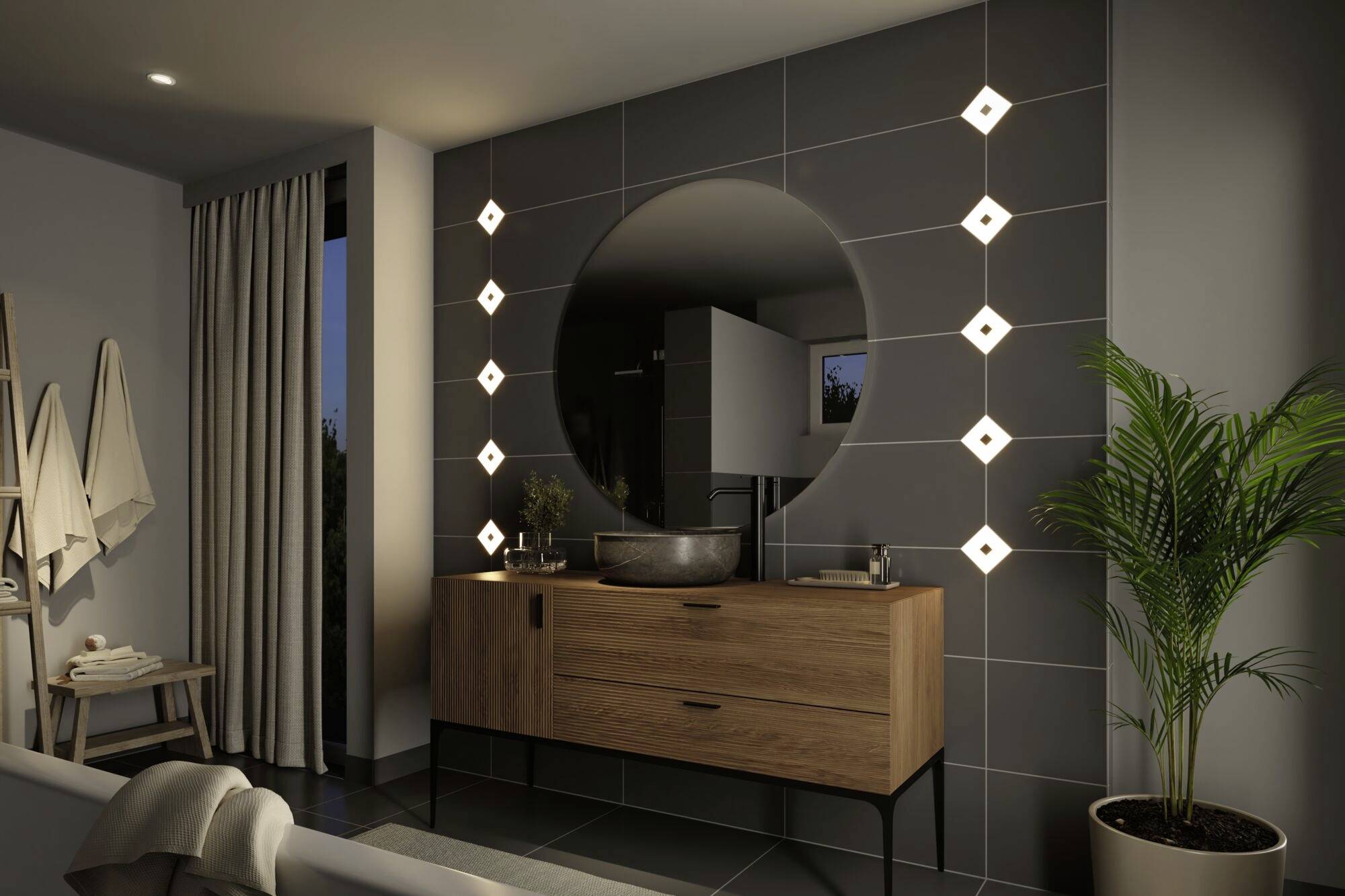 Une salle de bain moderne avec un grand miroir rond, entouré de lumières décoratives. Un meuble-lavabo en bois en dessous et une plante d'intérieur à côté.