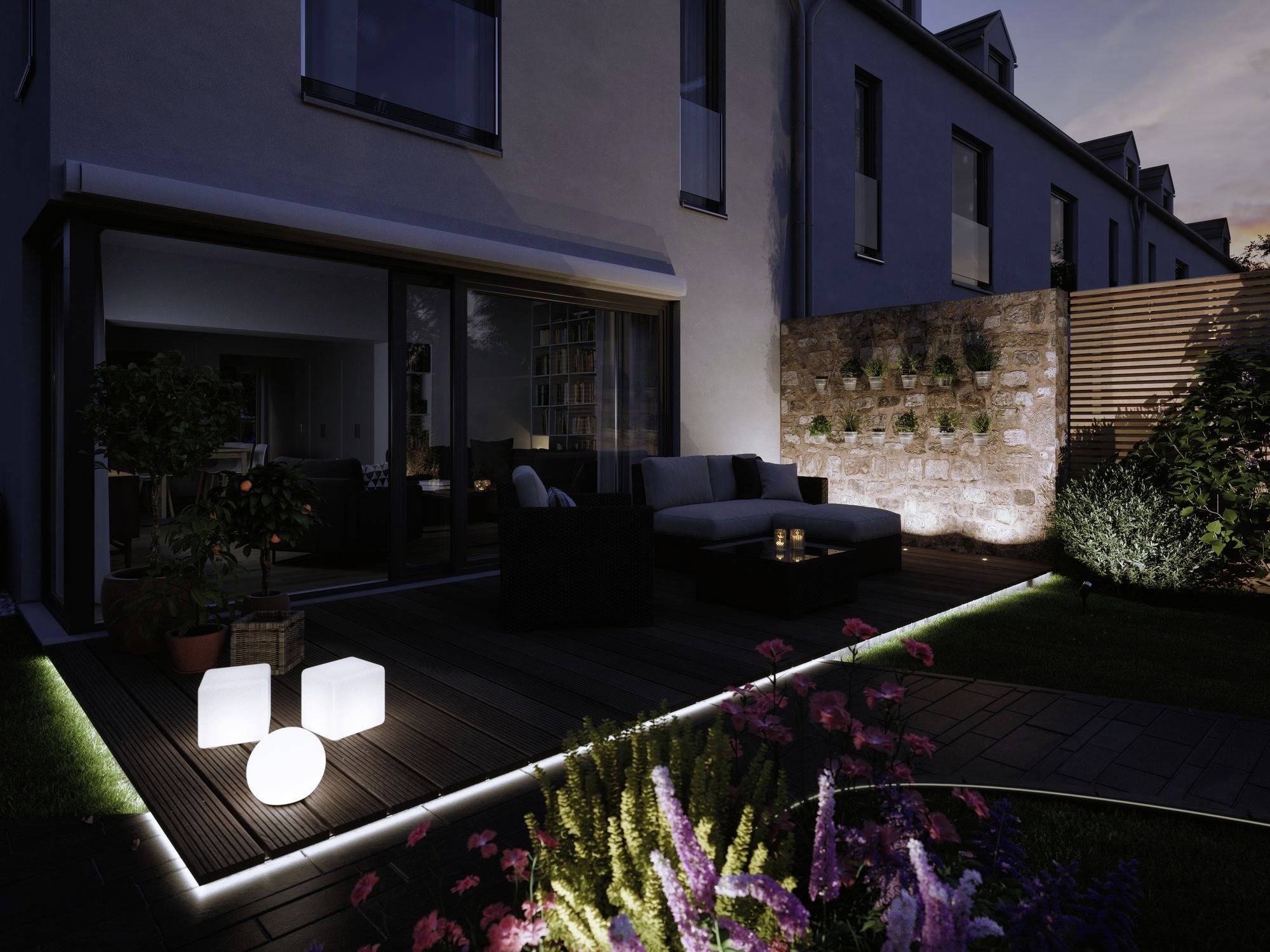 Une terrasse moderne de nuit, éclairée par des luminaires encastrés élégants. Des meubles et un mur végétalisé sont visibles en arrière-plan.