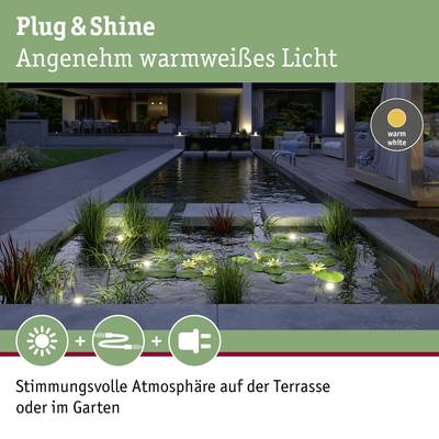 Une terrasse de nuit, éclairée par des lumières blanc chaud, entourée de plantes et d'eau, crée une atmosphère agréable.