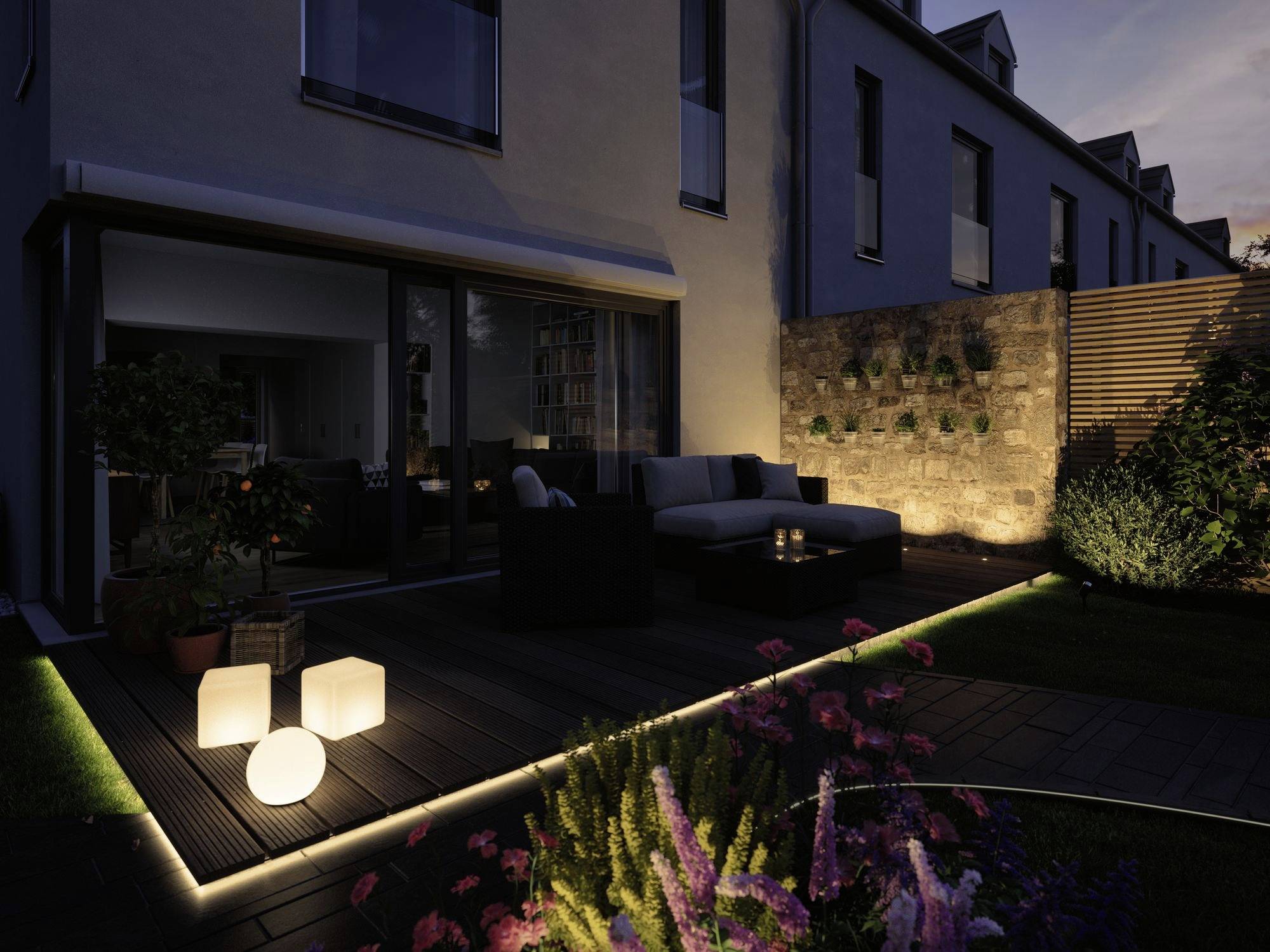 Jardin au crépuscule, éclairé de manière moderne avec du mobilier extérieur, des plantes et des luminaires décoratifs. Ambiance chaleureuse et accueillante.