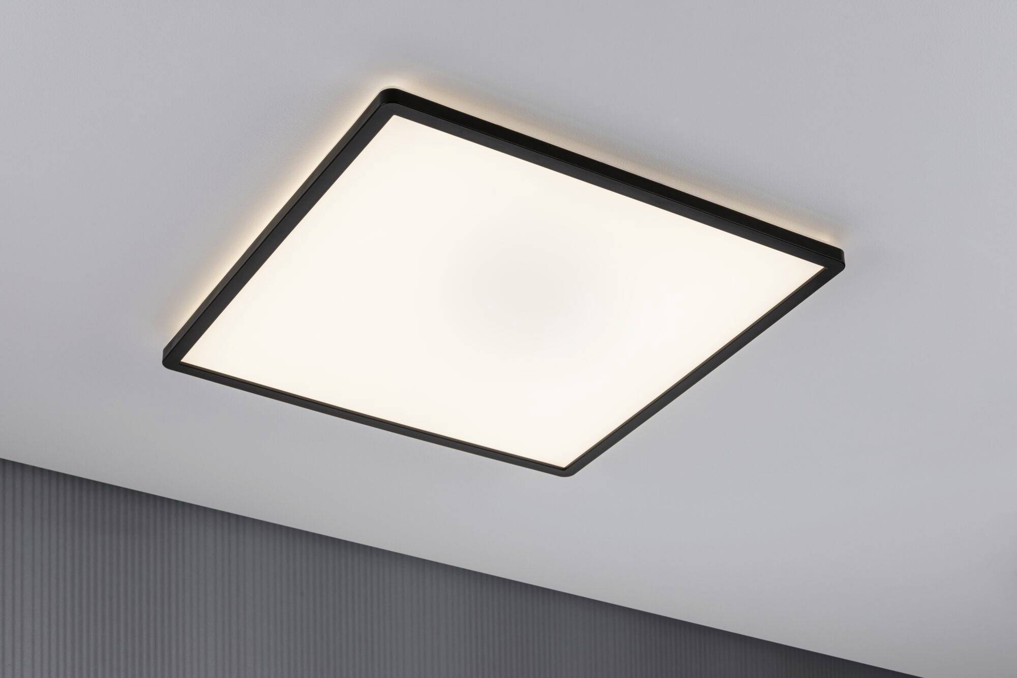 Plafonnier carré avec un cadre noir sur un plafond gris, diffusant une lumière blanche diffuse.