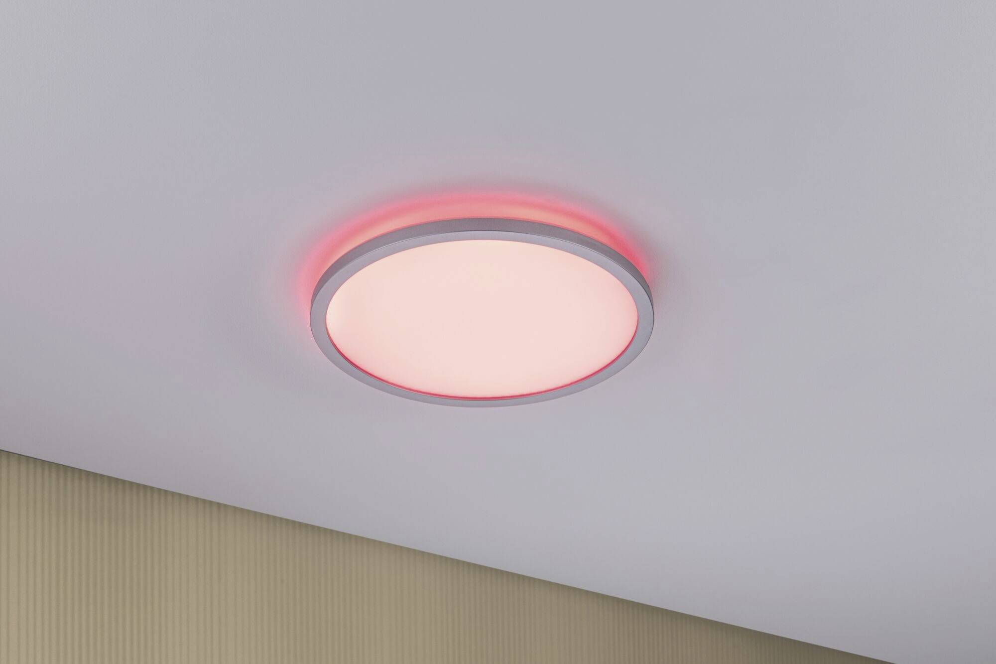Luminaire rond au reflet rouge fixé au plafond blanc au-dessus d'une section de mur beige.