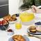 Une table avec un petit-déjeuner : Une main verse du jus d'orange dans un verre. À côté, des croissants, des fraises, de la confiture, un petit pain et des myrtilles.