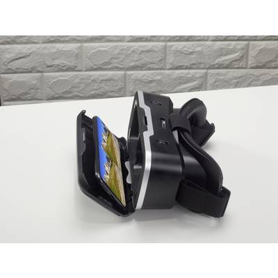 Casque de réalité virtuelle sur une table blanche, ouvert avec un smartphone affichant un paysage montagneux. Mur de briques en arrière-plan.