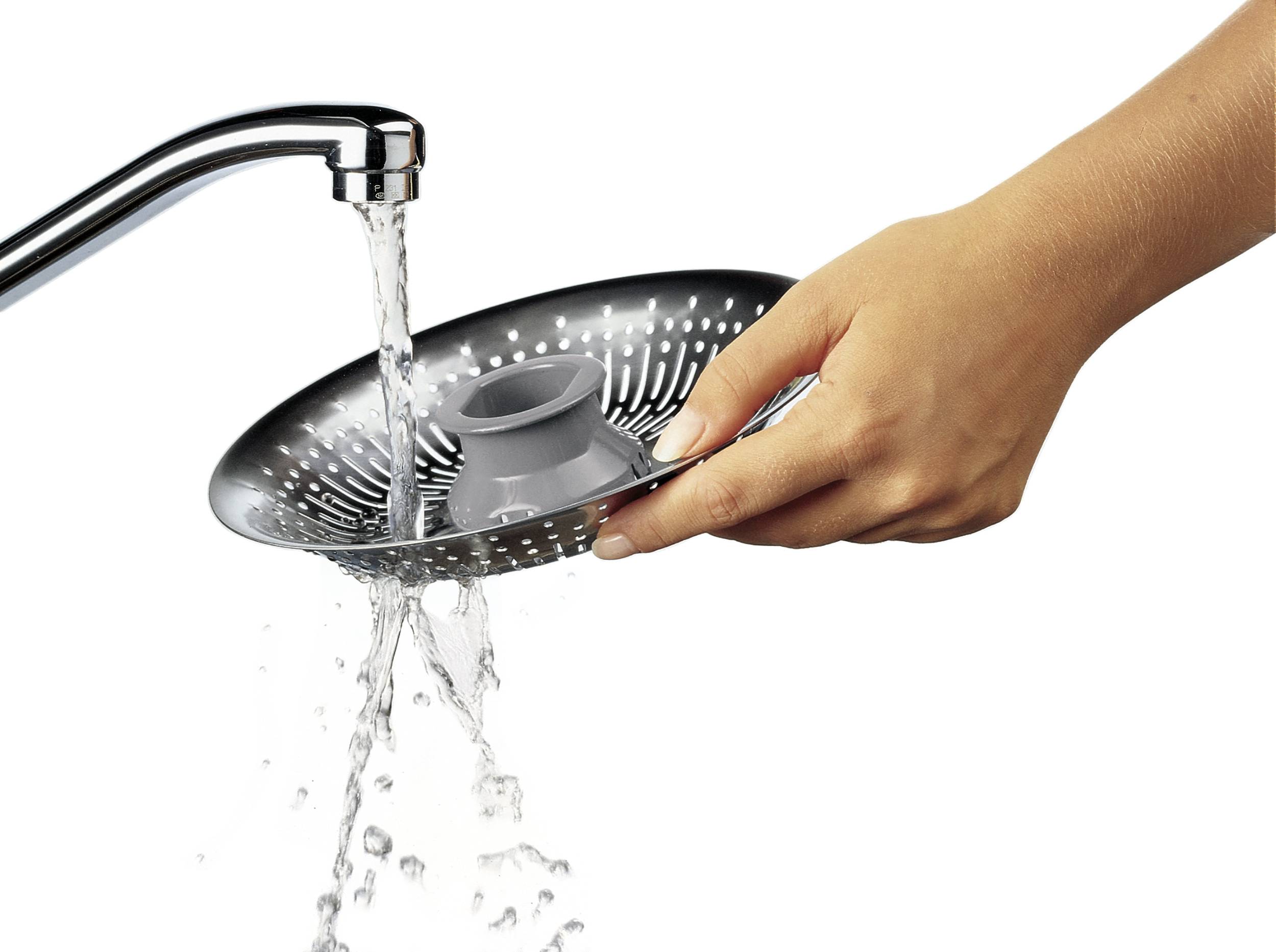 Une main tient un tamis métallique rond sous un robinet. L'eau coule à travers le tamis, permettant de rincer des aliments.