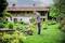 Un homme entretient la pelouse dans le jardin d'une maison de campagne traditionnelle. Les alentours sont verdoyants et fleuris.
