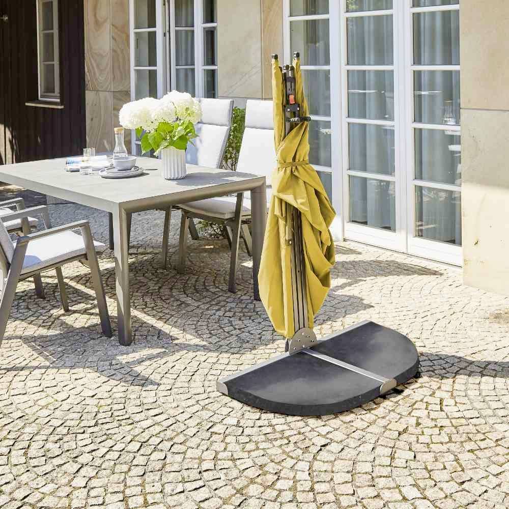 Une cour ensoleillée avec une table, six chaises et un parasol jaune. Sur la table, il y a un vase rempli de fleurs blanches.