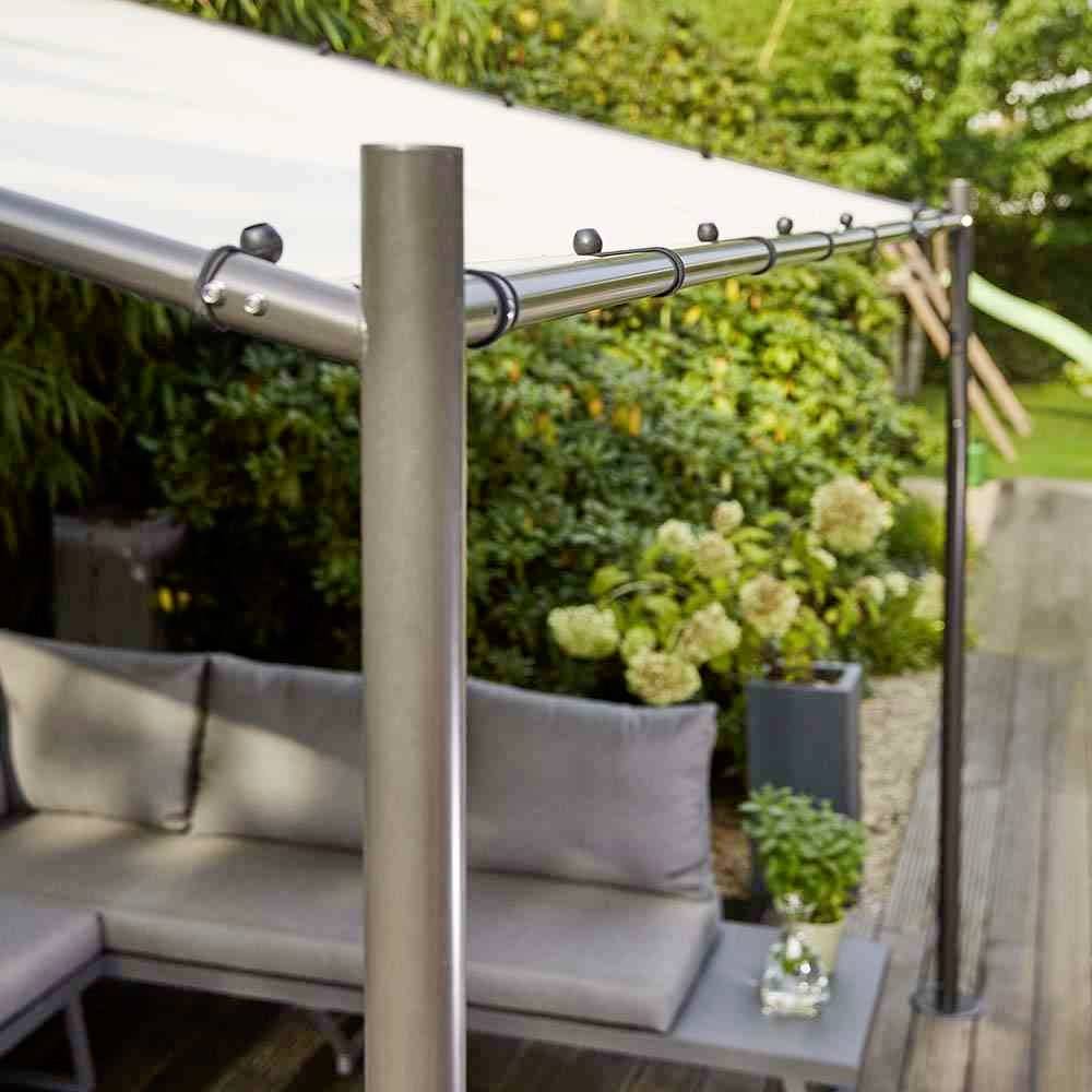Une pergola moderne avec une voile solaire blanche. En dessous, un canapé gris et des plantes en arrière-plan.