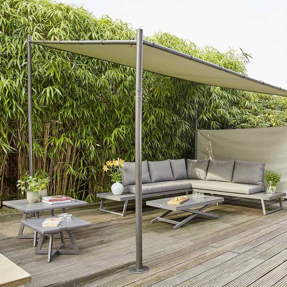 Salon de jardin avec canapé gris, table et parasol, entouré de plantes de bambou sur une terrasse en bois.