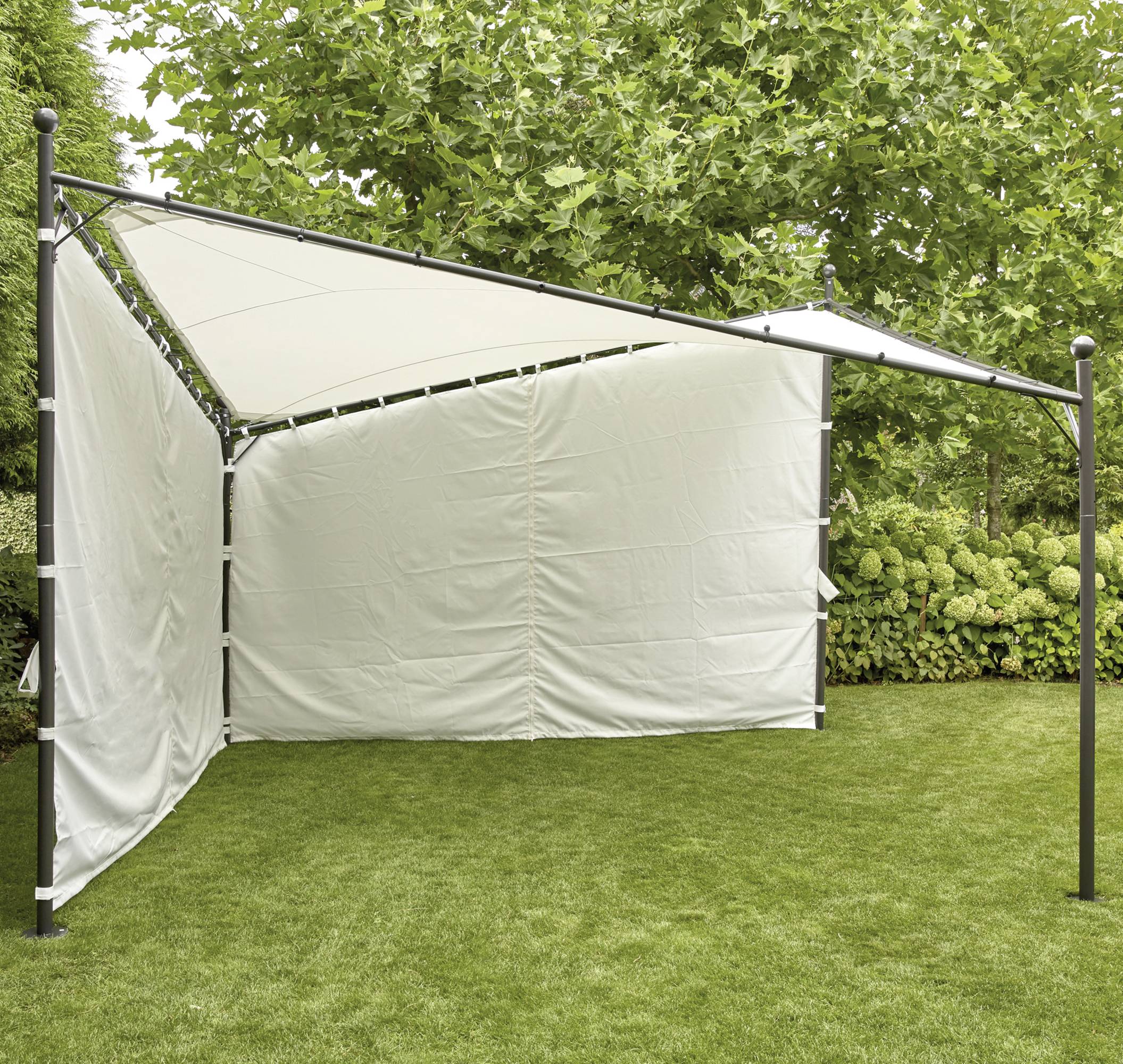 Un voile d'ombrage blanc avec une couverture latérale en tissu, tendu au-dessus d'une structure rectangulaire en métal, est installé dans un jardin verdoyant.