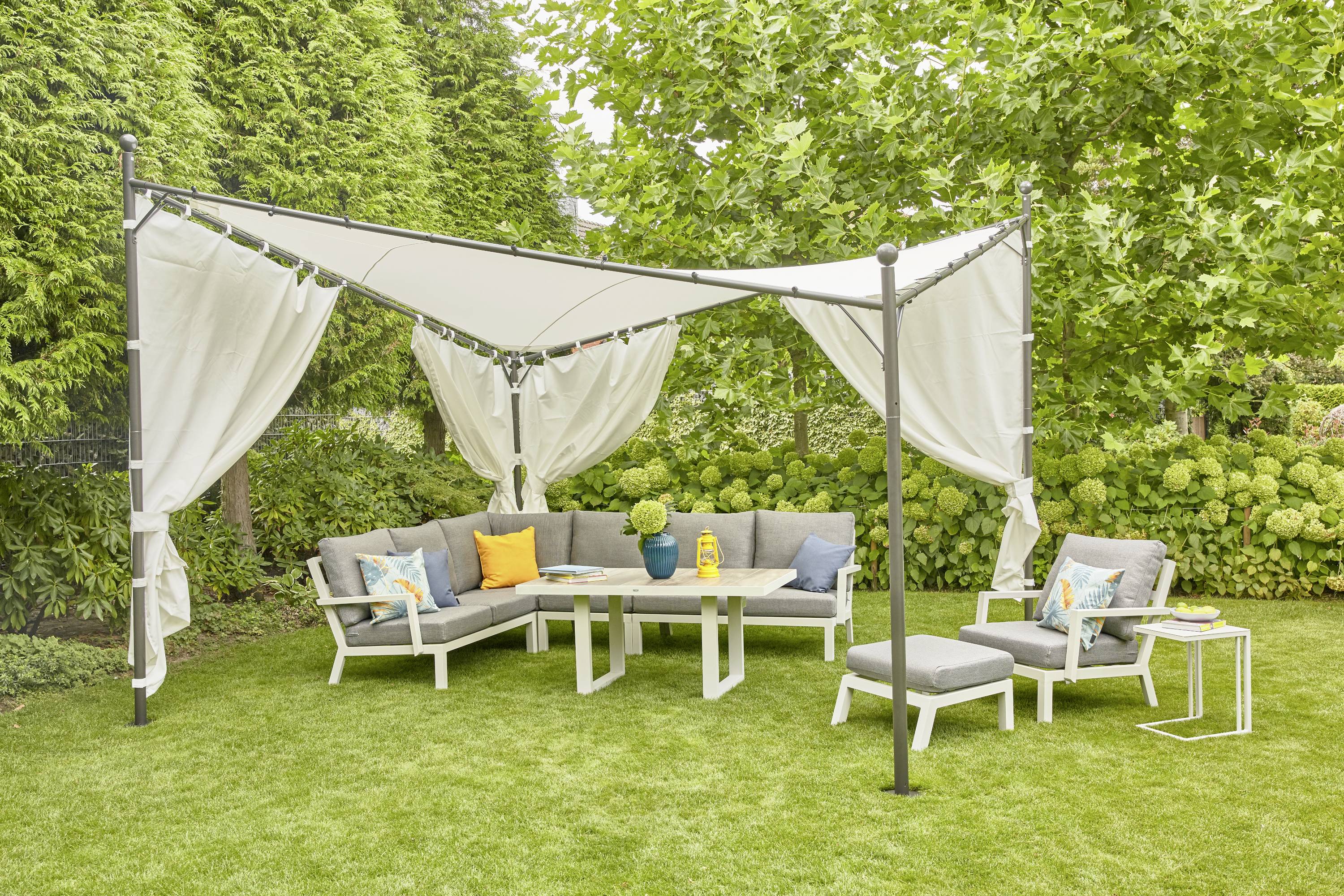'Coin salon dans le jardin sous un pavillon avec des rideaux blancs, entouré de verdure. Des canapés gris et des coussins colorés offrent un espace de détente confortable.'