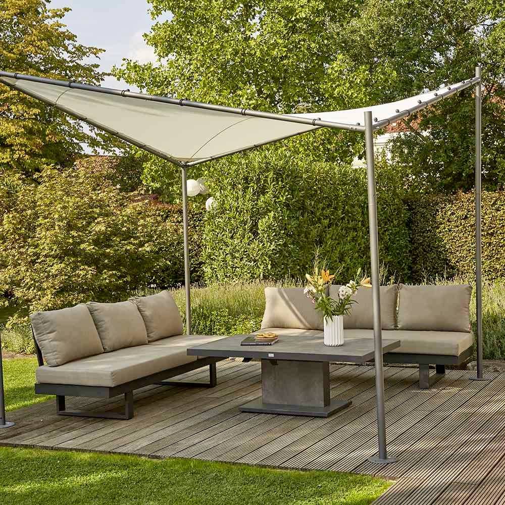 Une terrasse avec des meubles de jardin gris et une voile d'ombrage blanche. À l'arrière-plan, on aperçoit des haies vertes et des arbres.