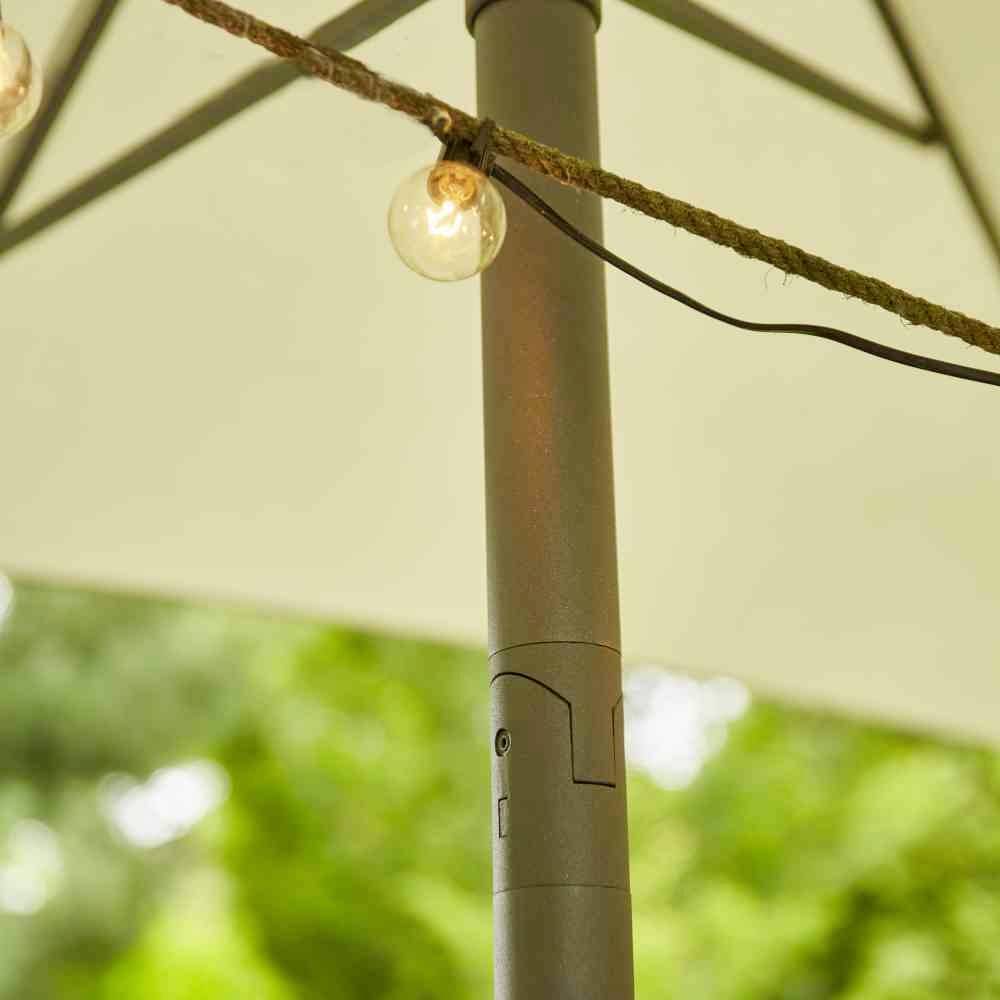 Un parasol avec une guirlande lumineuse, des arbres verts flous en arrière-plan, créant une atmosphère de jardin paisible.