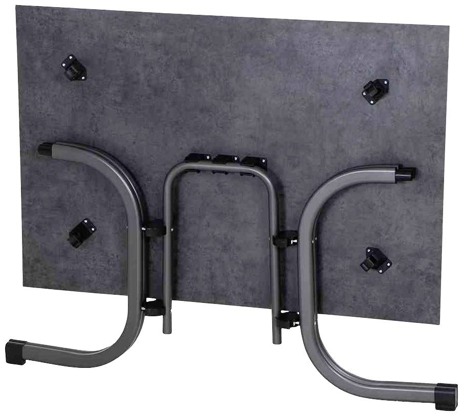 Une table rectangulaire rabattue avec des pieds en métal et un plateau sombre, qui montre le mécanisme de fixation des pieds.