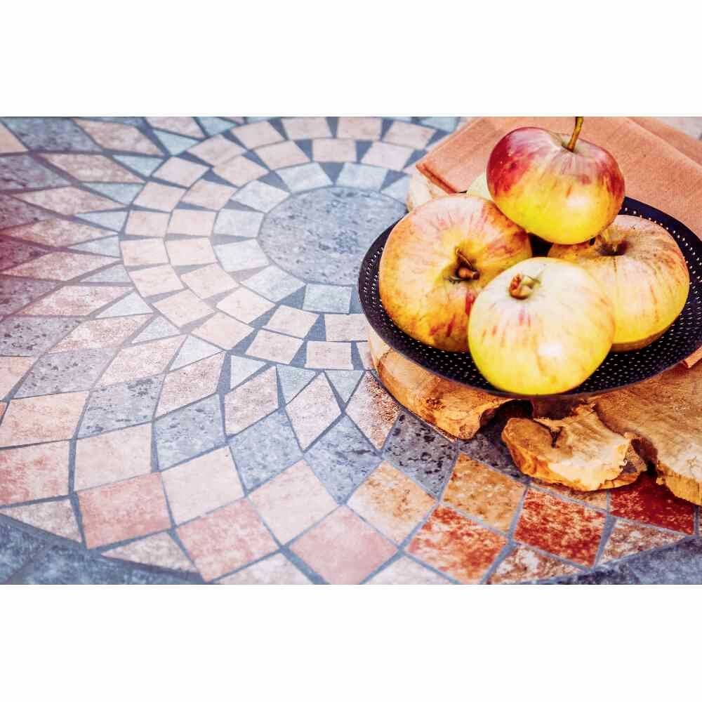 Trois pommes sont posées sur une planche en bois ronde, placée sur un sol à motif de mosaïque.