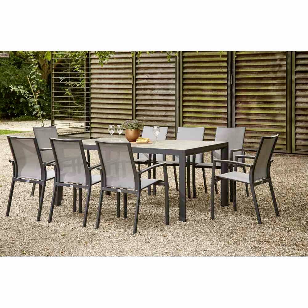 Ensemble de meubles de jardin : Table rectangulaire moderne avec huit chaises en métal et plastique, installé sur une surface de graviers et entouré d'un habillage en bois.