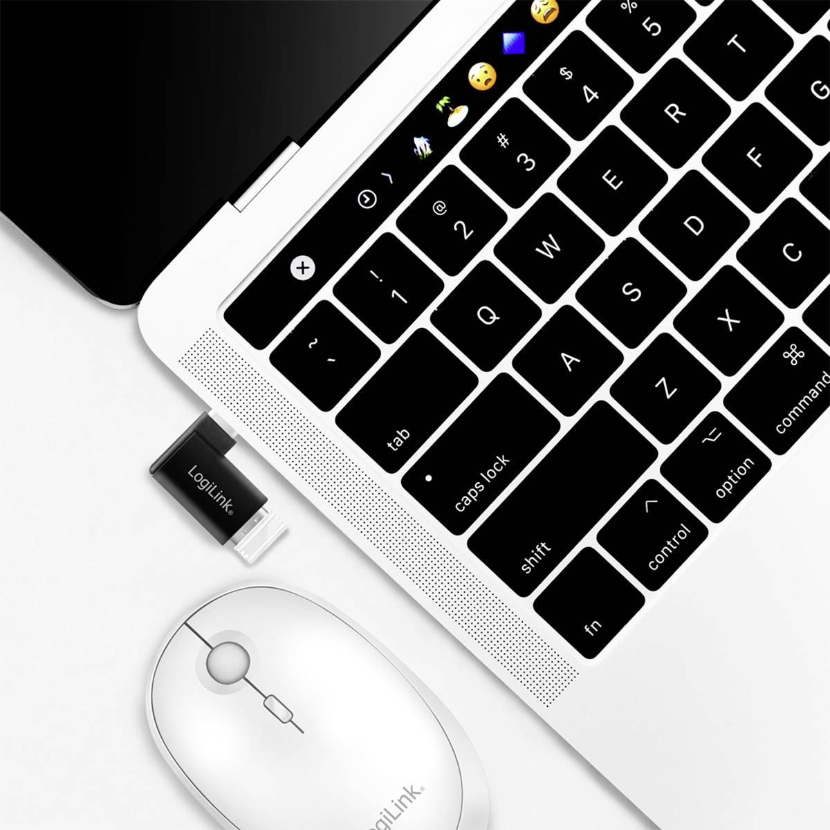 Une souris sans fil Logitech et un récepteur USB sont posés à côté d'un clavier d'ordinateur portable ouvert sur un fond blanc.