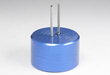 Un condensateur métallique cylindrique bleu avec deux bornes sortant vers le haut, posé sur une surface blanche.