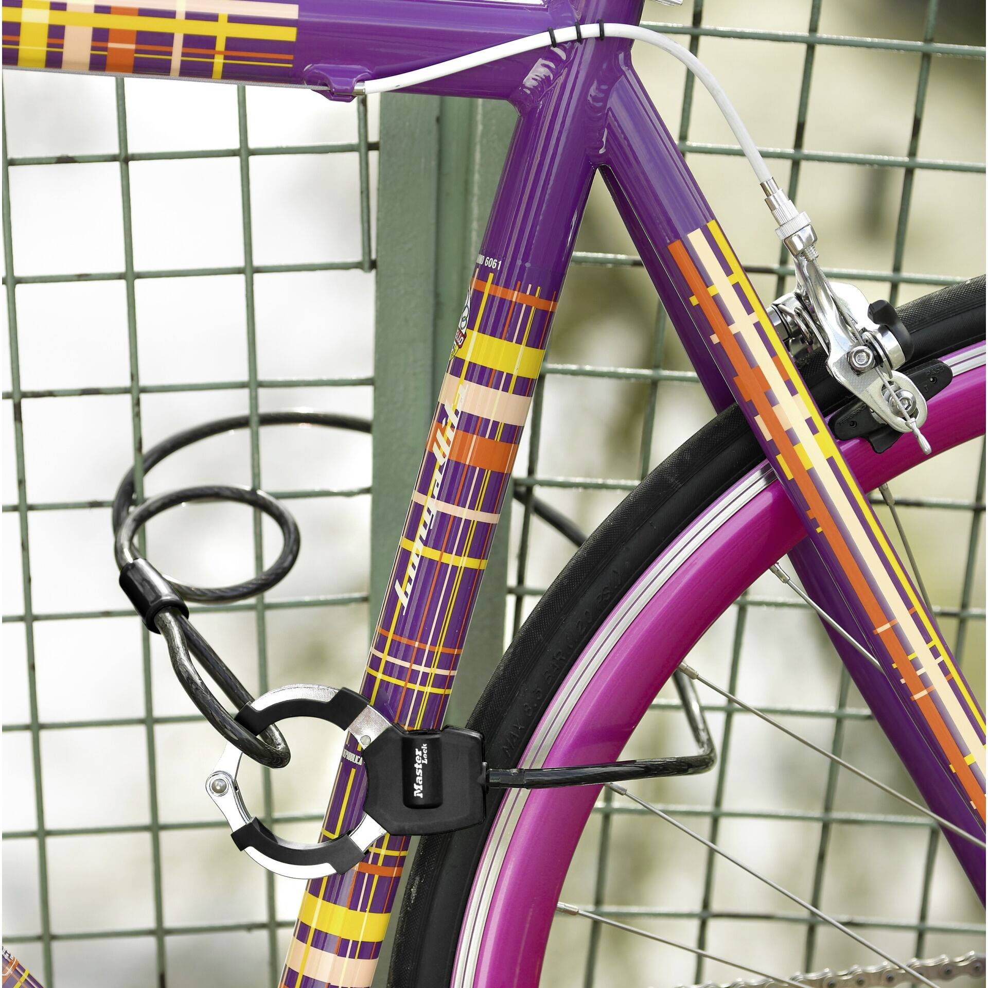 Vélo à carreaux lilas et jaunes avec un pneu rose, attaché par un cadenas à une rambarde métallique.