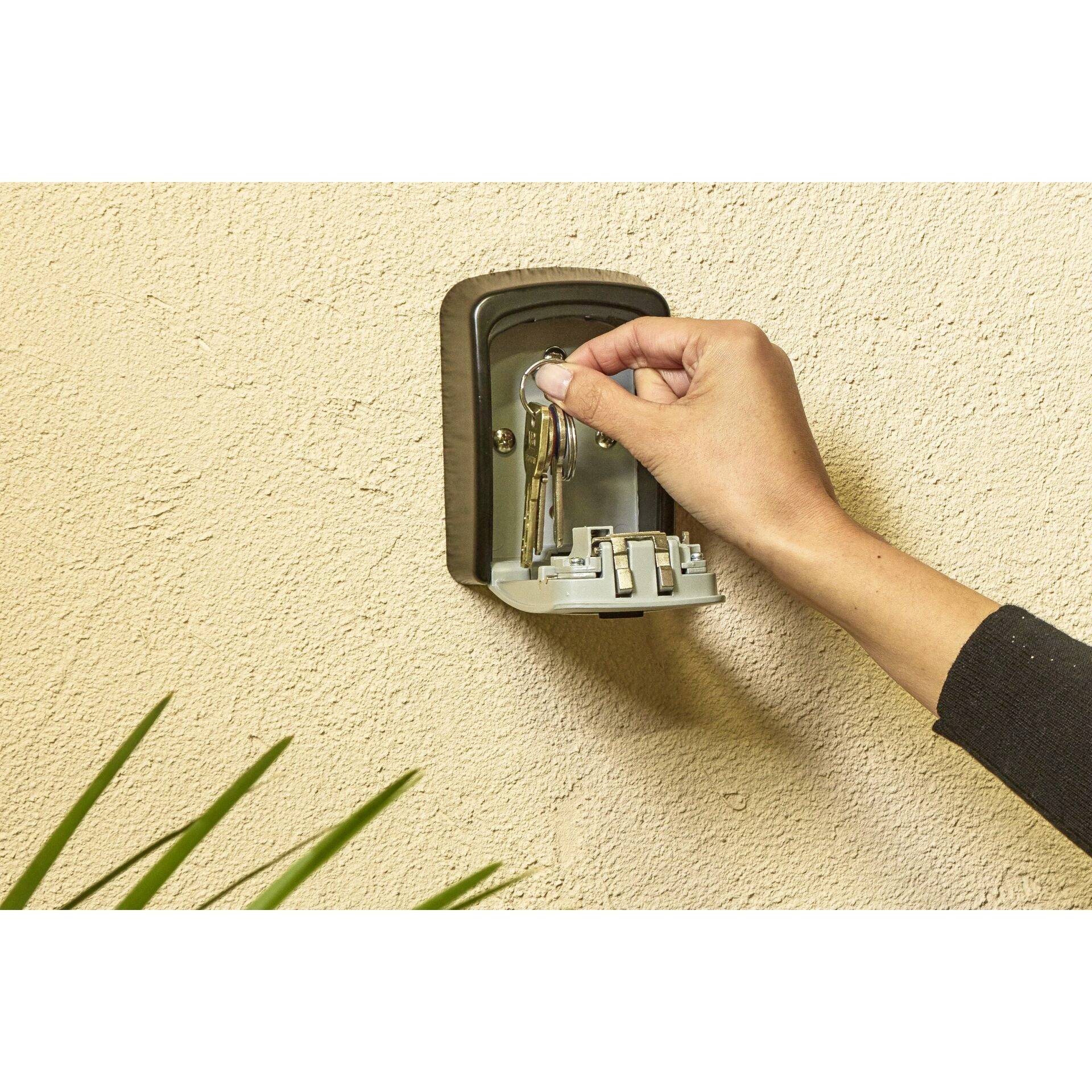 Une main ouvre un coffre-fort à clés fixé au mur et en retire une clé.