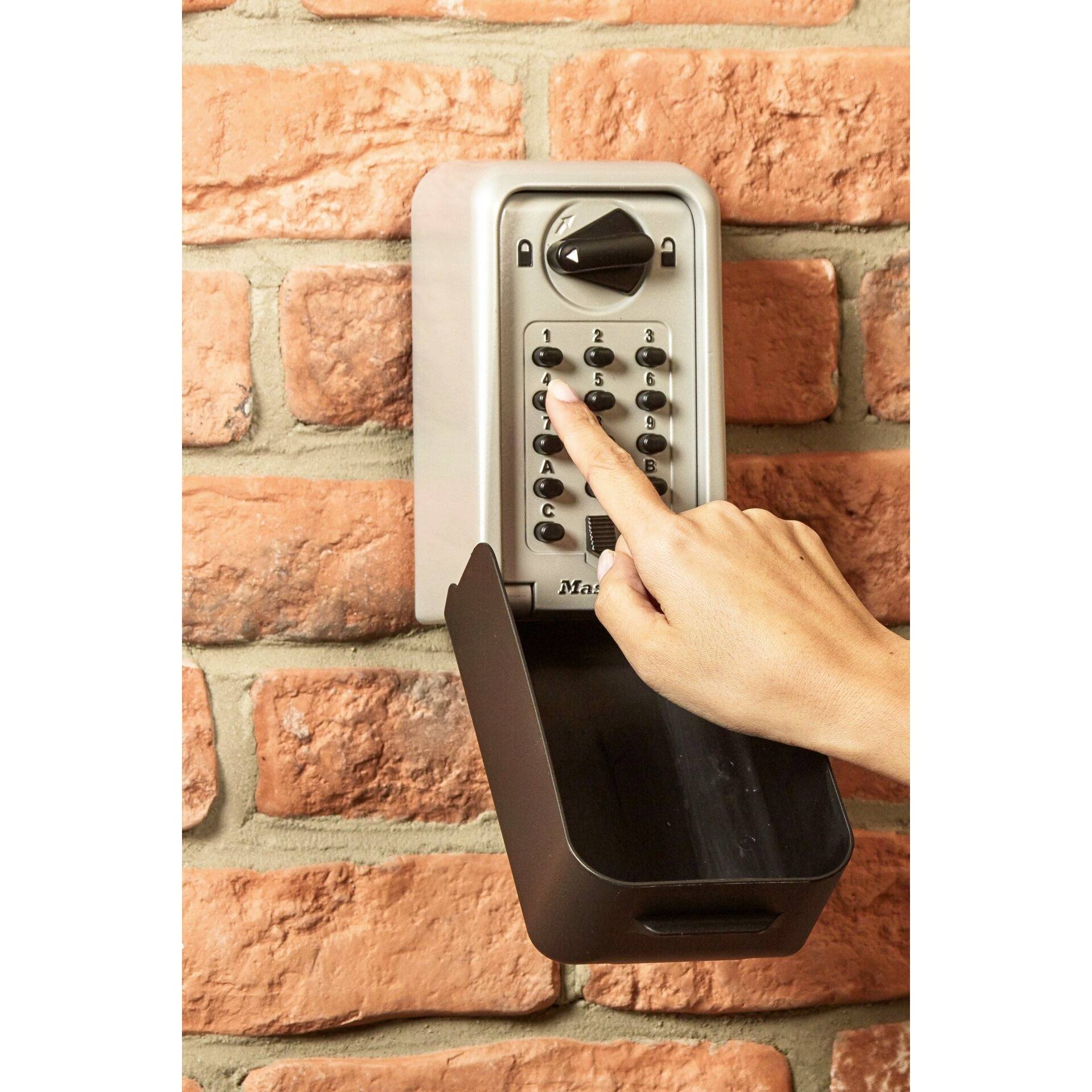Un doigt pointe sur les touches d'un clavier de serrure de sécurité fixé à un mur de briques.