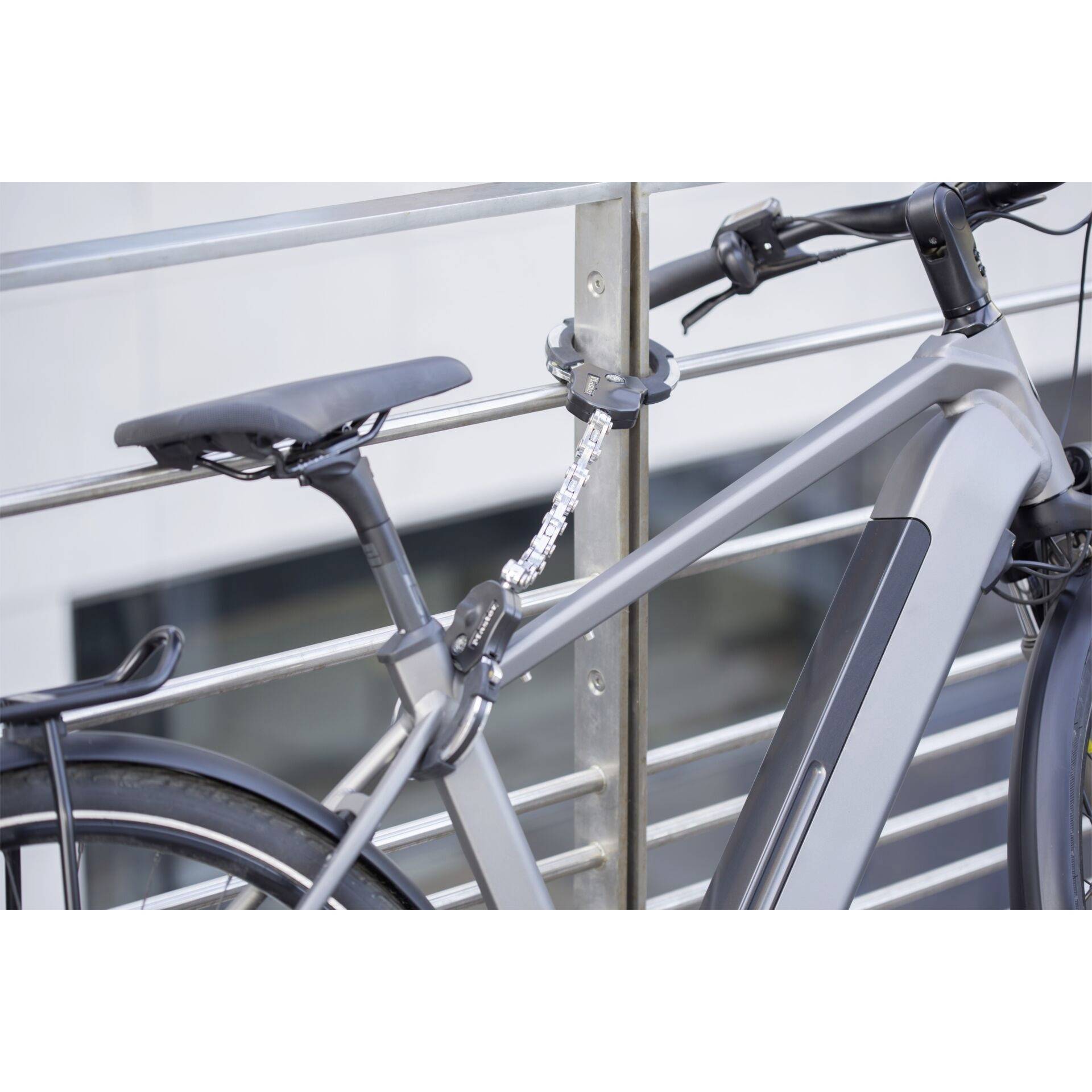 Vélo gris solidement attaché à une barrière, dans un environnement urbain. Il est équipé d'un cadenas de sécurité contre le vol.