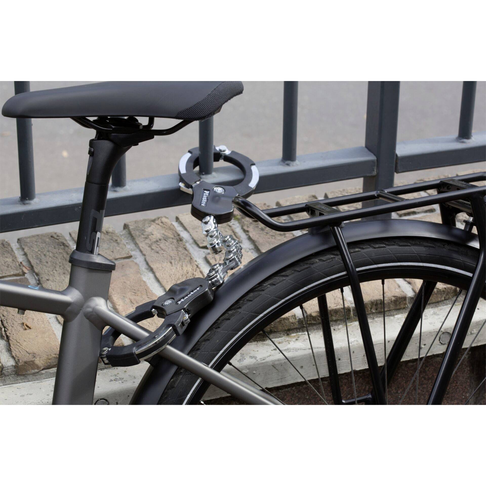 Un vélo attaché avec un câble-antivol à une grille métallique. La roue arrière est visible, ainsi que le porte-bagages noir.