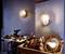 Espace de travail avec des outils et une table. Deux lampes murales brillantes éclairent la pièce. Au premier plan, un miroir doré est visible.