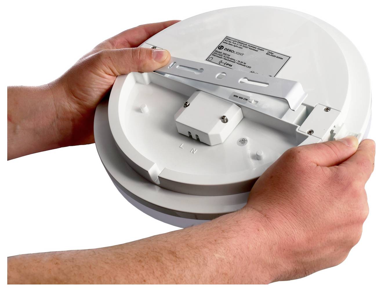 Des mains tenant l'arrière d'un détecteur de fumée rond, montrant son support de fixation et son connecteur électrique pour l'installation.