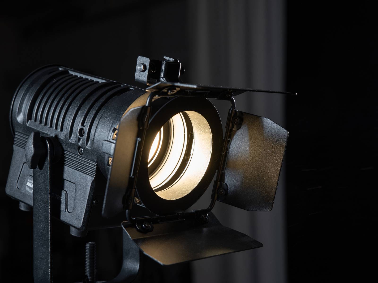 Un projecteur de studio noir avec des volets ouverts projette une lumière vive et illumine une zone devant un arrière-plan sombre.