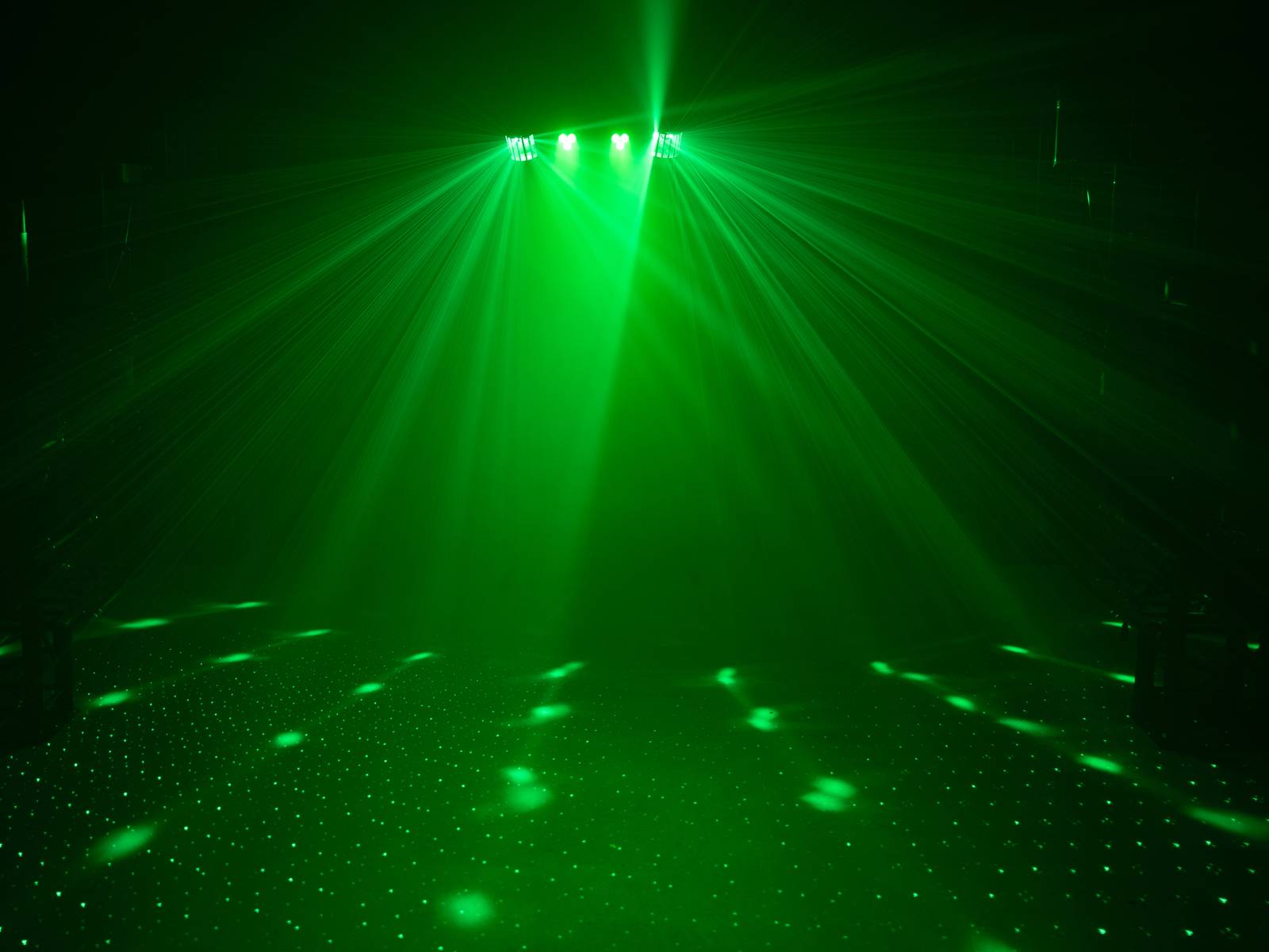 Une lumière verte de projecteur de scène illumine un espace vide avec des motifs rayonnants.