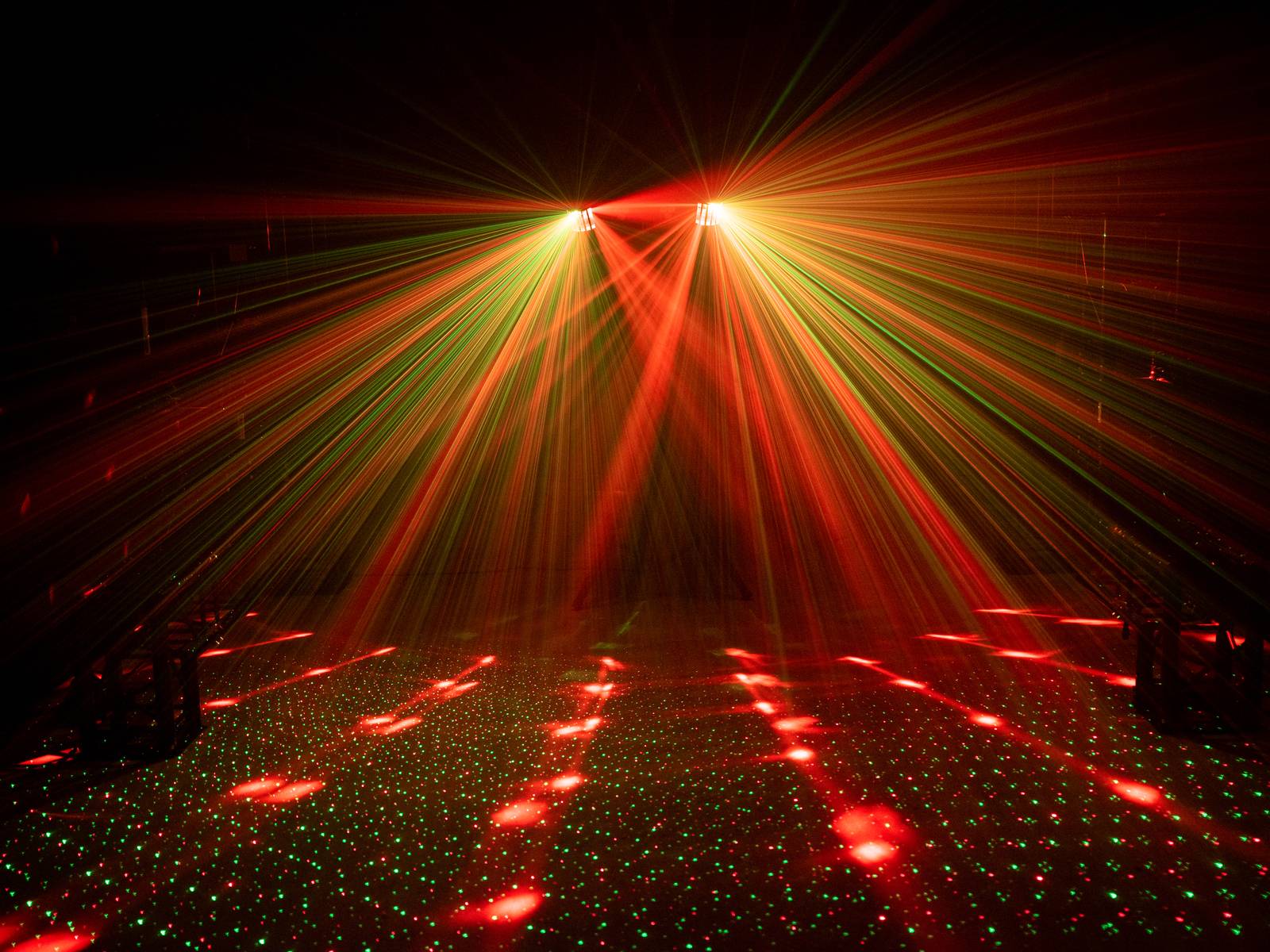 Spectacle lumineux avec des rayons laser rouges et verts formant un motif en quadrillage sur le sol et se propageant dans une pièce sombre.