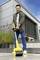 Un homme nettoie une terrasse avec un nettoyeur de sol jaune. Derrière lui se trouve un bâtiment moderne avec de grandes fenêtres et des plantes.