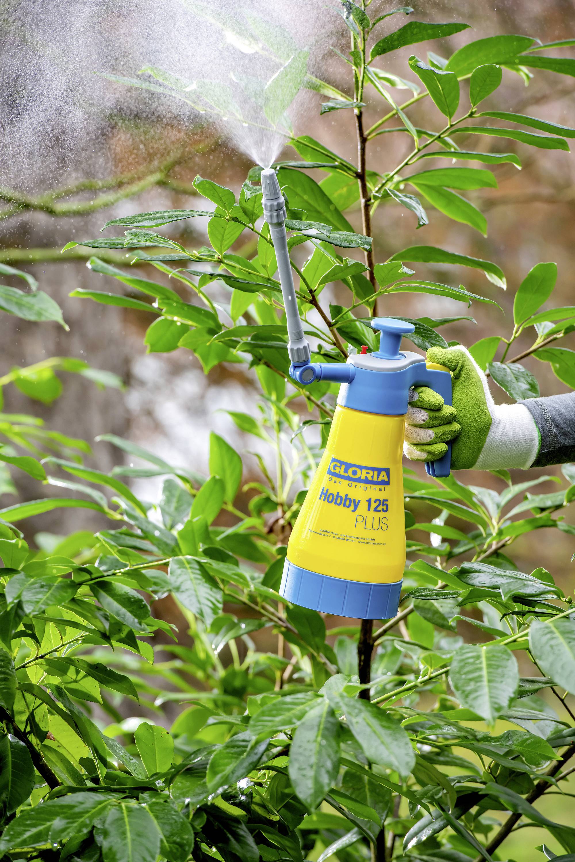 Une personne pulvérise une plante verte avec un pulvérisateur à main jaune.