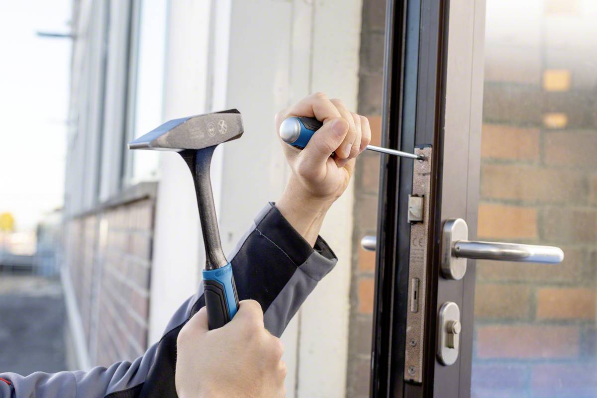Deux mains tiennent un marteau et un tournevis et travaillent sur une serrure de porte.