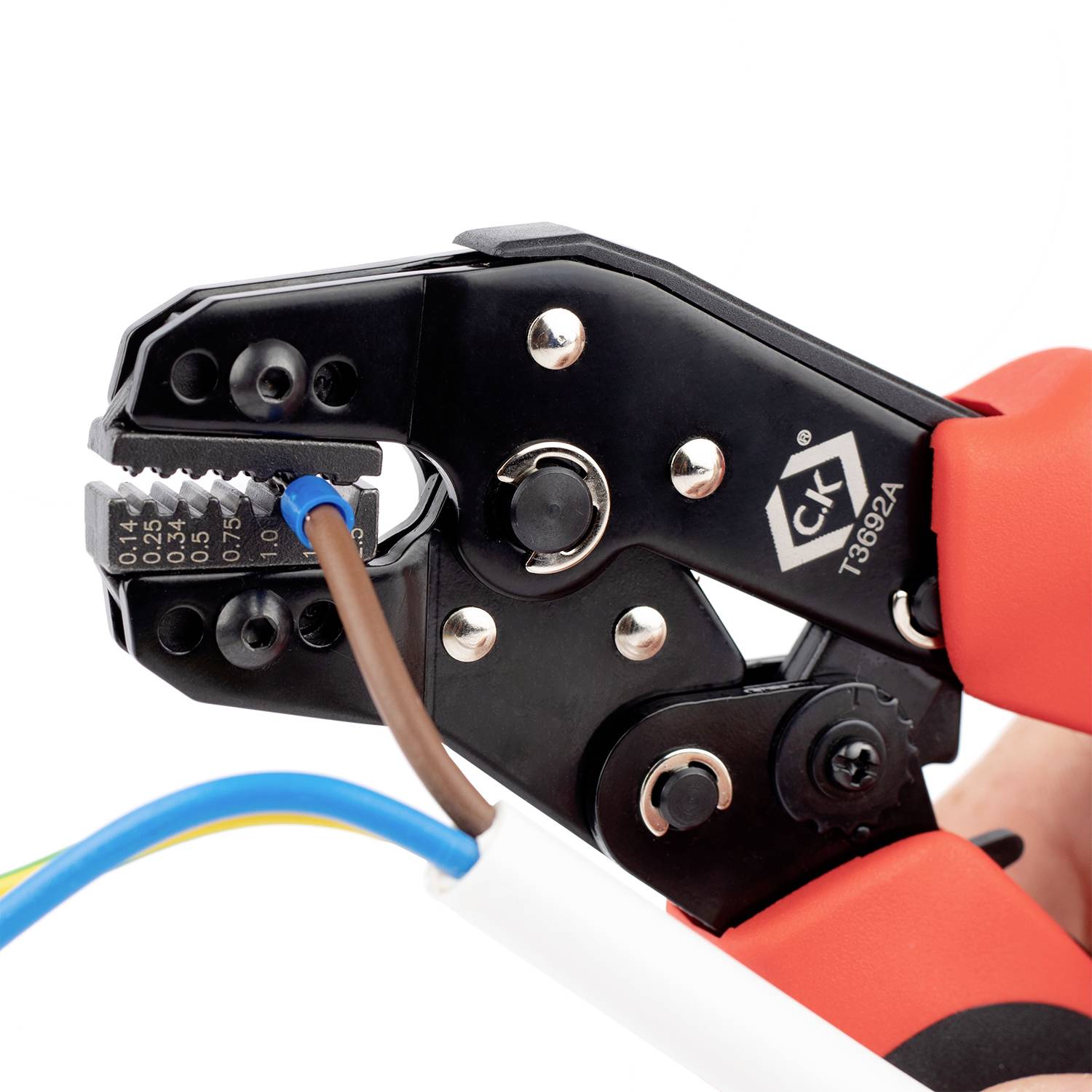 Une main tient une pince à sertir rouge en train de traiter l'extrémité d'un câble aux conducteurs isolés.