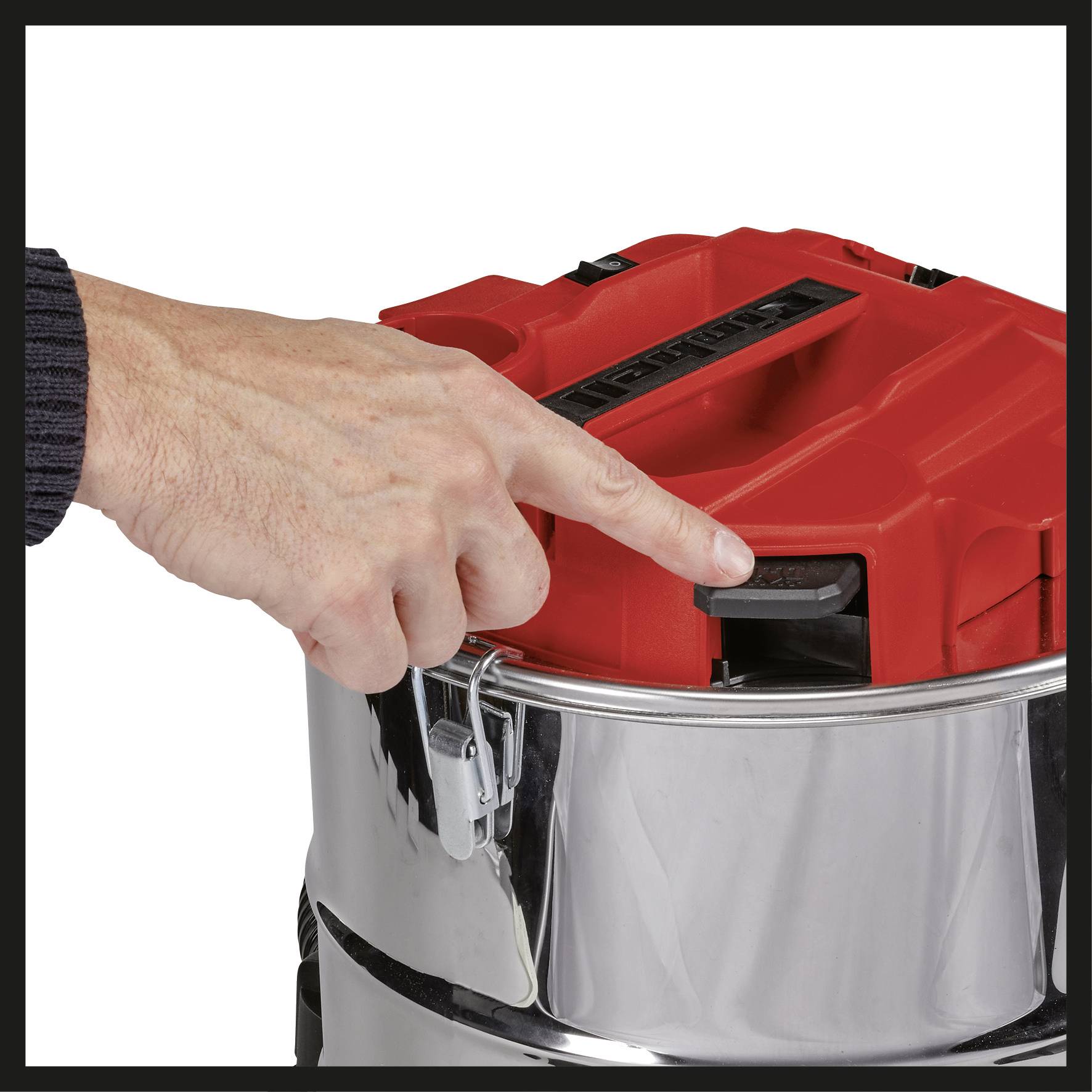 Une main appuie sur un bouton rouge d'un récipient argenté fermé, avec des attaches sur les bords.