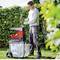 Un homme en vêtements de travail utilise un broyeur de végétaux pour déchiqueter des branches dans un jardin. Des haies sont visibles en arrière-plan.