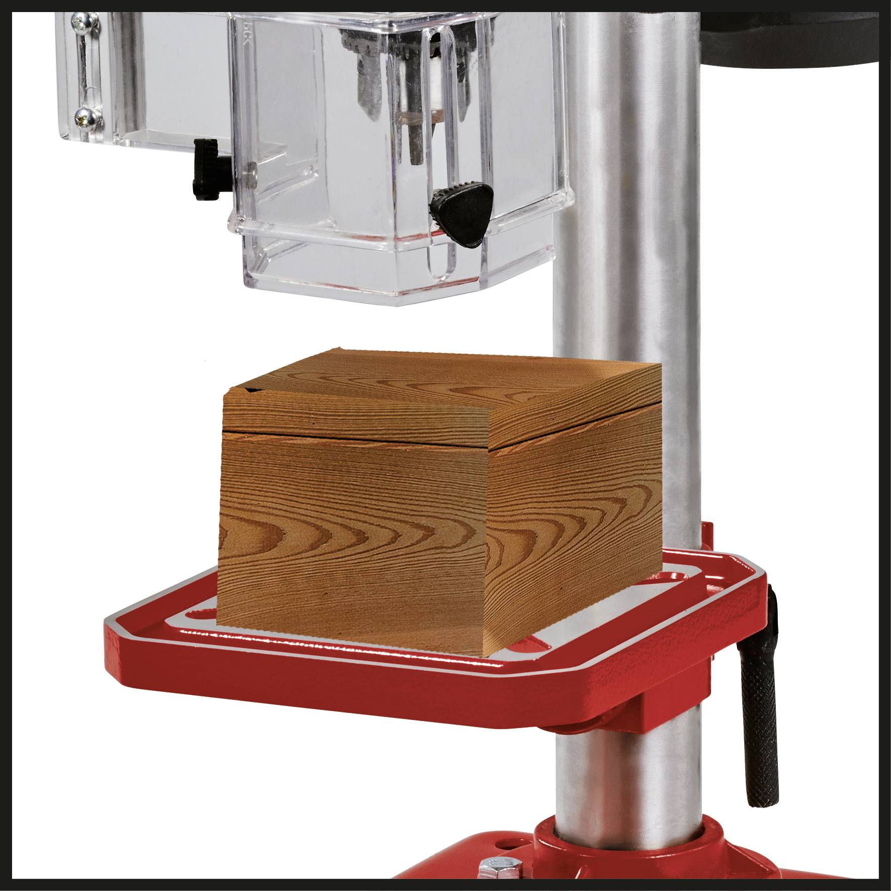 Une perceuse avec un coffret en bois sur sa surface de support. La machine est argentée et rouge, le coffret est en bois clair.