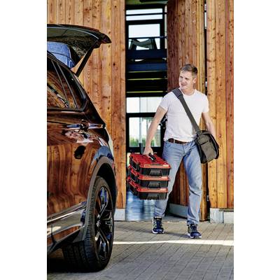 Un homme en jeans et t-shirt tient deux coffres à outils rouges et se dirige vers une voiture dont le coffre est ouvert. L'entrée d'un bâtiment est visible en arrière-plan.