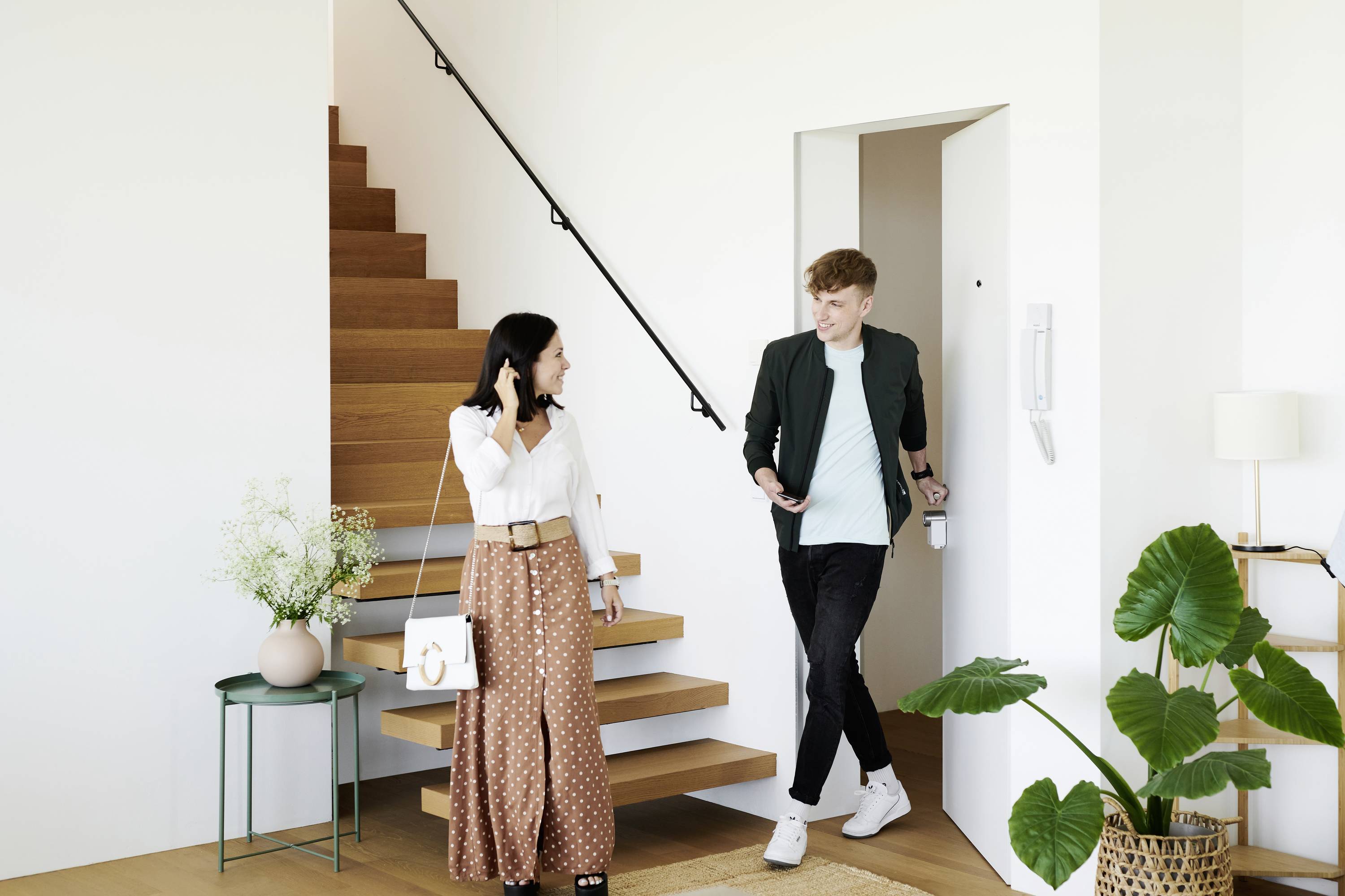Une femme et un homme discutent dans un salon moderne à côté d'un escalier en bois. Tous deux semblent détendus et sourient.