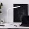 Bureau avec une lampe blanche moderne, un ordinateur portable, un carnet de notes, un stylo et de petites plantes. Environnement de travail minimaliste et relaxant.