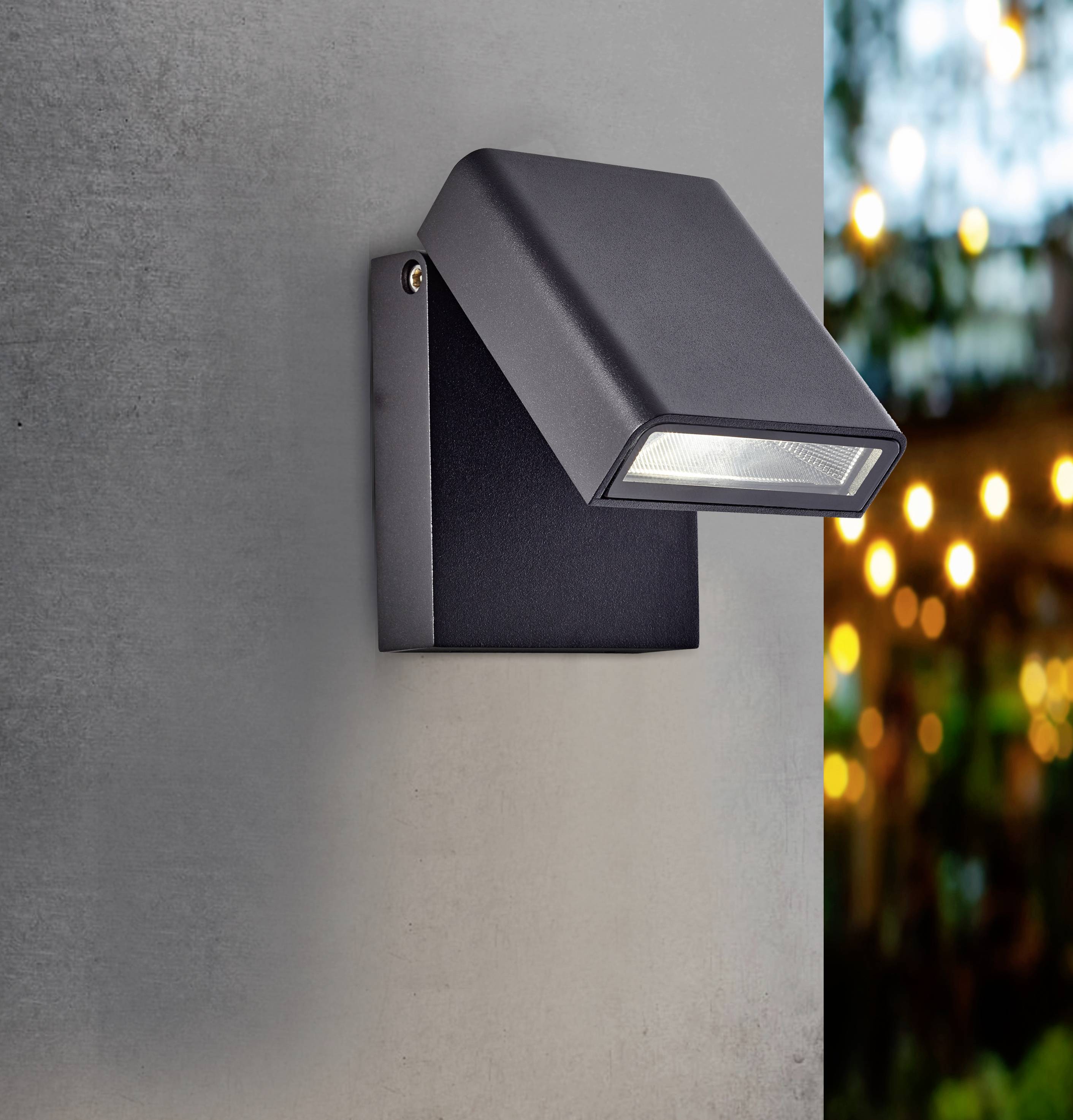 Applique murale extérieure au design moderne qui diffuse une lumière blanc chaud et illumine un mur en béton ; des lumières floues sont visibles en arrière-plan.