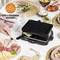 Un grill à raclette sur une table, prêt pour quatre personnes. Il y a de la salade, des cornichons marinés, un assortiment de viandes et de fromages.
