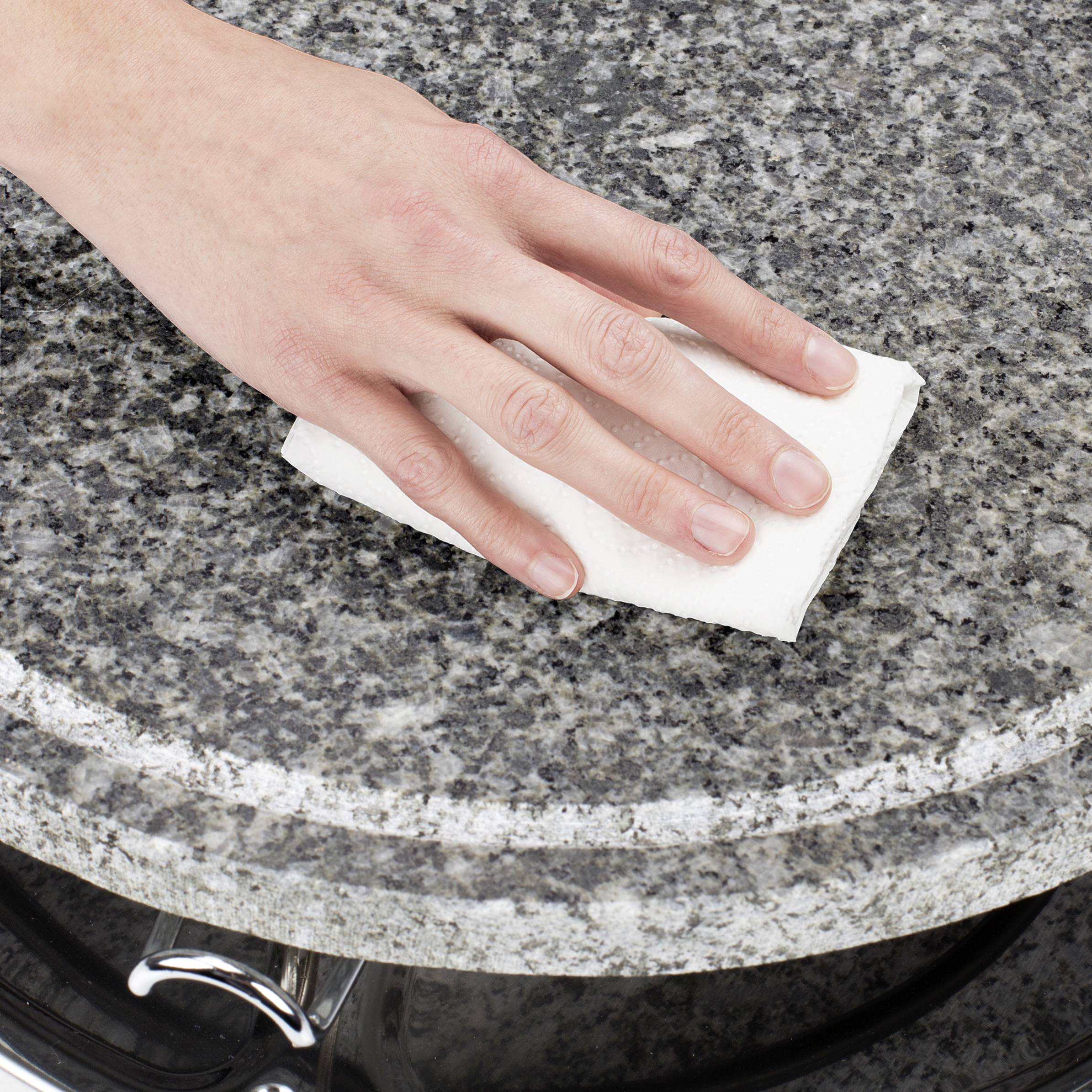 Une main nettoie une surface en granit avec un chiffon blanc.
