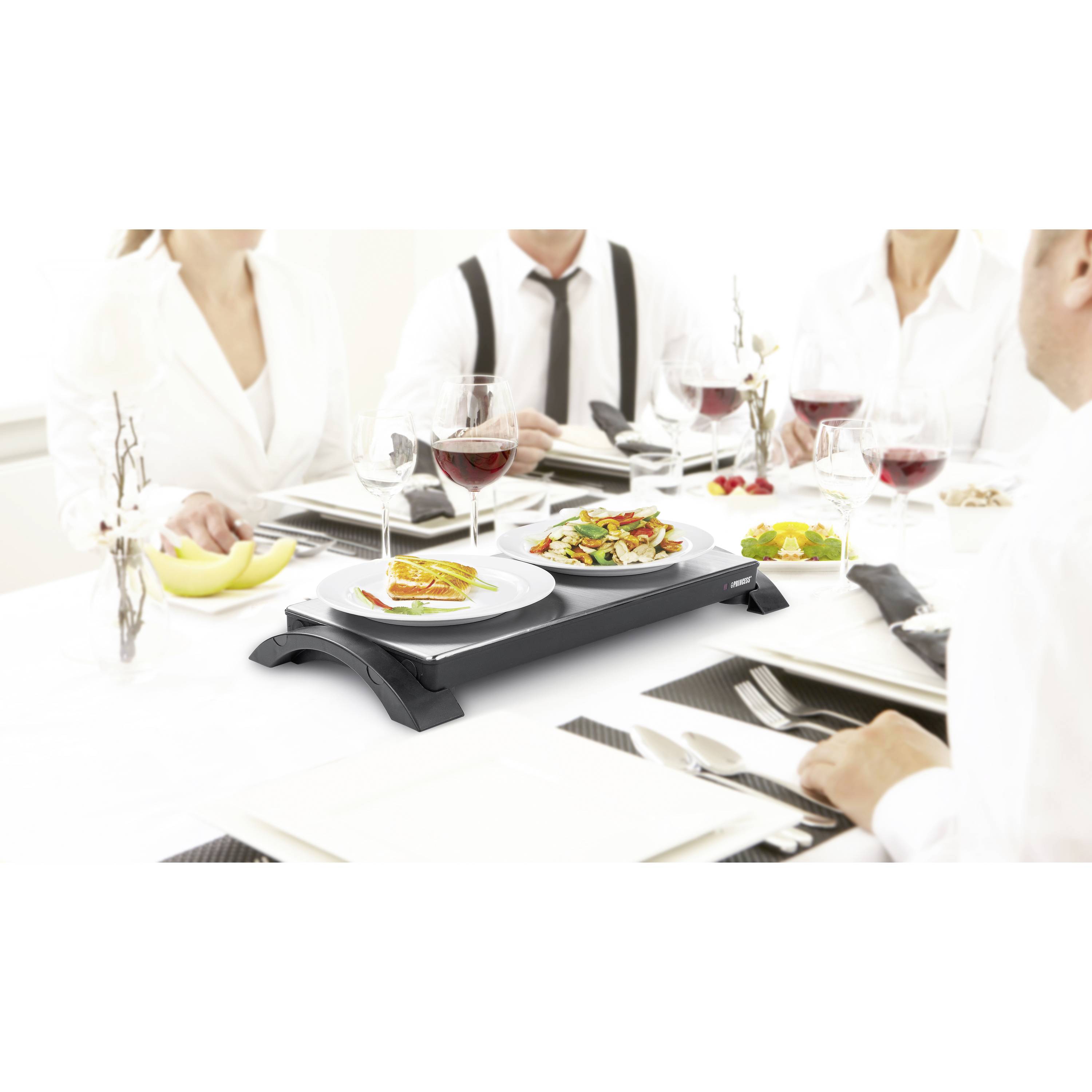 À table dressée de manière festive, des personnes vêtues de blanc sont assises. Sur la table, des assiettes garnies de mets et des verres de vin rouge sont disposés.